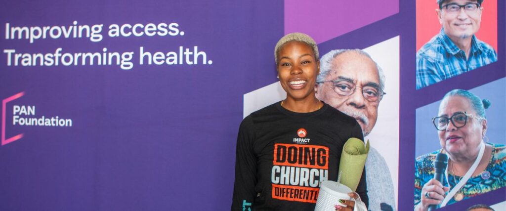 A smiling festival attendee standing in front of a PAN Foundation banner